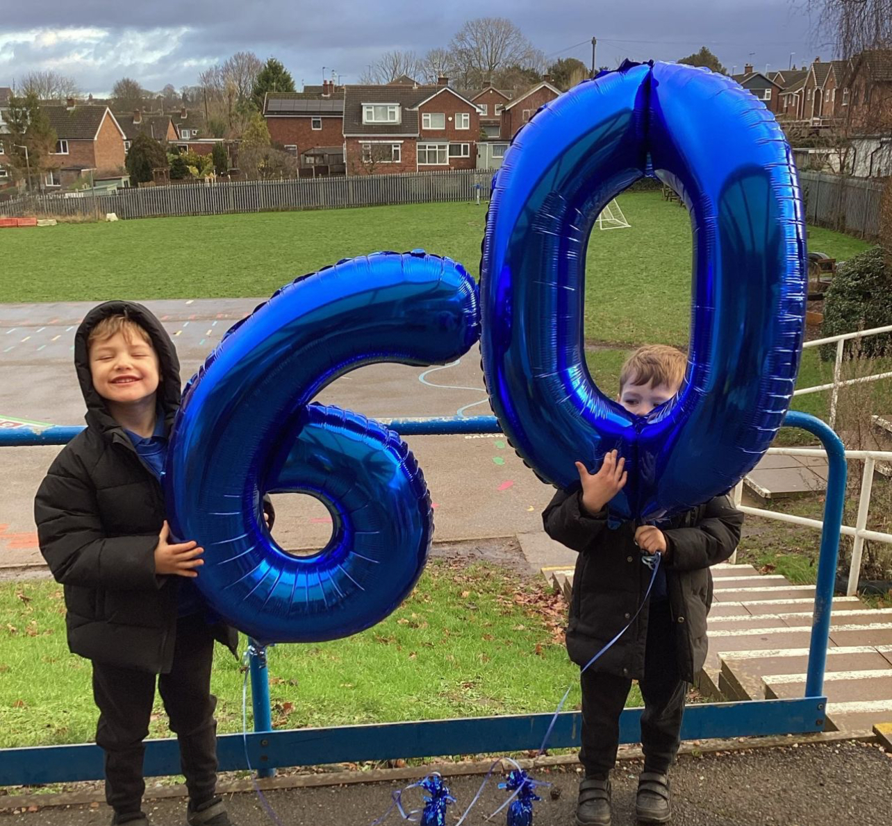 Two school children hold balloons depicting 60